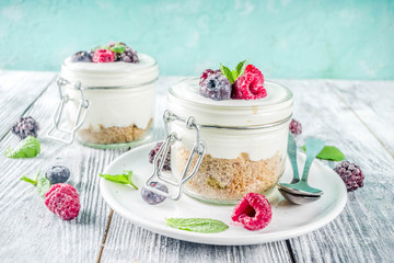 Recipe ideas for summer diet breakfast, healthy morning dessert Cheesecake in portioned jars with summer berries - raspberry, blueberry, blackberry. On wooden background copy space
