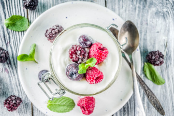Recipe ideas for summer diet breakfast, healthy morning dessert Cheesecake in portioned jars with summer berries - raspberry, blueberry, blackberry. On wooden background copy space