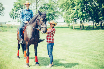 Couple riding a horse in the farm in cowboy style. Sport, happiness, hobby concept
