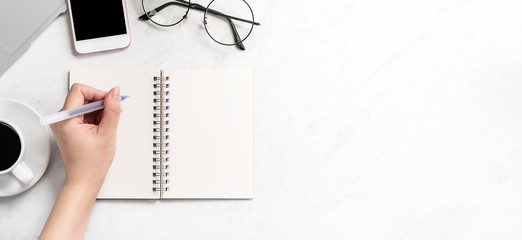 A woman is writing notes isolated on stylized marble office working desk with smartphone, laptop, glasses and coffee, mock up, topview, flatlay, copyspace, closeup