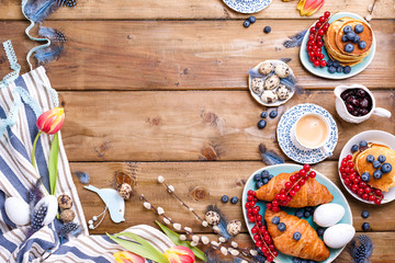 Easter breakfast flat lay with fresh coffee, berries and pastries , orange tulips, croissants with bacon and various sweets , colored quail eggs and spring holidays decorations. Top view. Copy space.