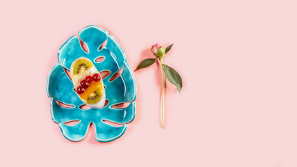 Fruit dessert cake with spring flowers of the pion on a blue ceramic plate, isolated on pink background. Top view. Copy space