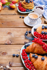 croissant with currant and blueberry berries, fresh aromatic coffee on a wooden table. Continental breakfast with fresh sweet pastries. Free space for text.
