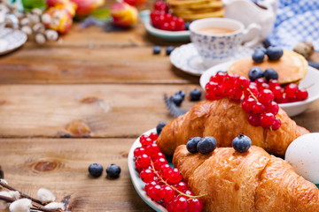 croissant with currant and blueberry berries, fresh aromatic coffee on a wooden table. Continental breakfast with fresh sweet pastries. Free space for text.
