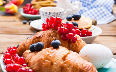 croissant with currant and blueberry berries, fresh aromatic coffee on a wooden table. Continental breakfast with fresh sweet pastries. Free space for text.