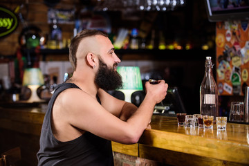 Hipster brutal man drinking alcohol ordering more drinks at bar counter. Guy spend leisure in bar with alcohol. Man drunk sit alone in pub. Alcoholism and depression. Alcohol addicted concept