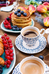 Fresh aromatic coffee in a vintage cup, homemade pastries for breakfast with blueberries and currants, on a wooden background and spring tulips. Free space for text.