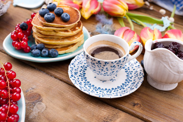 Fresh aromatic coffee in a vintage cup, homemade pastries for breakfast with blueberries and currants, on a wooden background and spring tulips. Free space for text.