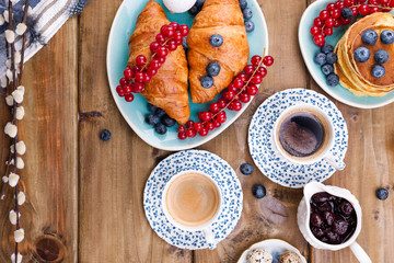 croissant with currant and blueberry berries, fresh aromatic coffee on a wooden table. Continental breakfast with fresh sweet pastries. Free space for text.