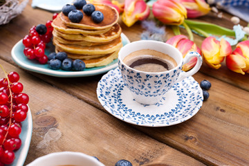 Fresh aromatic coffee in a vintage cup, homemade pastries for breakfast with blueberries and currants, on a wooden background and spring tulips. Free space for text.