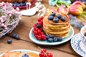 Homemade pastry croissant for breakfast with blueberries and currants and coffee, on a wooden background and spring tulips. Free space for text.
