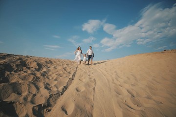 Cheerful caucasian family in white clothes with pretty daughter runs on desert sand dune. Pregnant woman