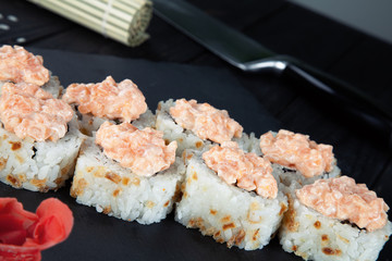 Close up view on sushi rolls with with red fish, okra and Philadelphia cheese on a black coal board and a wooden background. Traditional Japanese cuisine. Food with copy free space for text, logo.