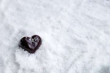 Assorted milk and dark chocolate heart on snow with copy space, Black Valentine's Day concept.