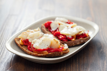 black healthy bread with cod fish and red pepper on dish