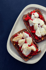 black healthy bread with cod fish and red pepper on dish