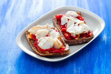 black healthy bread with cod fish and red pepper on dish