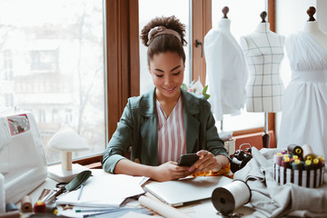 Chatting with clients. Young woman tailor with smartphone is answering