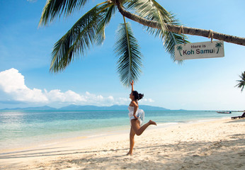 The girl in a white dress jumps to the palm trees on the beach of Samui Island