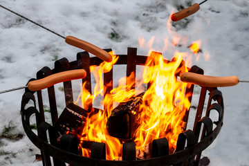 Closeup of a campfire with hot dog food over open fire. Winter snow outdoor scene.