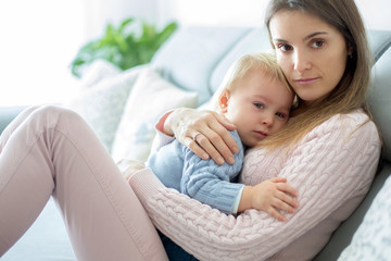 Young mother, holding her sick toddler boy, hugging him at home