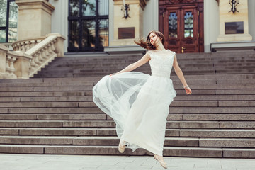 Fototapeta premium Gorgeous elegant caucasian young lady posing outdoors in old town in fashionable wedding dress. Beauty, fashion, vogue concept