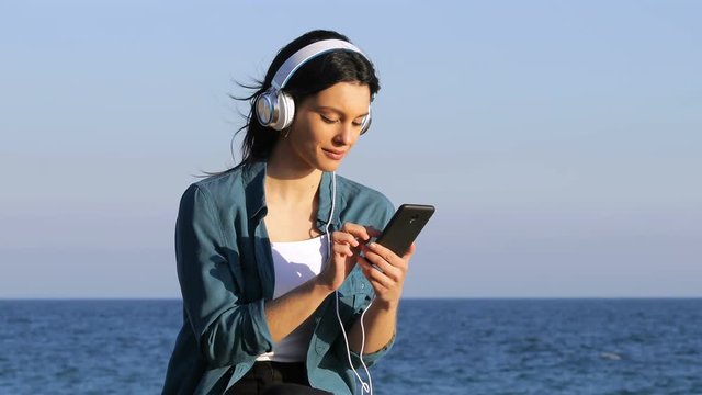 Happy woman relaxing listening to music from smart phone on the beach