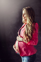 Fototapeta premium Pregnant woman in jeans holds hands on belly on a black background. Pregnancy, maternity, preparation and expectation concept. Close up, copy space, indoors. Beautiful tender mood photo of pregnancy