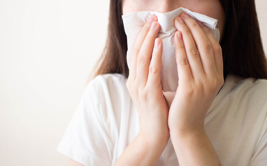 Young woman​ sneezing and blowing her nose w/ tissue​ paper. Cause of runny nose include common cold, flu, allergies, sinusitis, asthma, air pollution or influenza. Health care concept. Close up. - obrazy, fototapety, plakaty