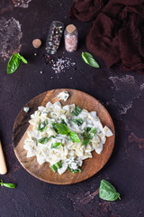 Pasta (farfalle) with creamy sauce with basil and gorgonzola cheese on a wooden plate. Dark brown concrete background. Copy space.