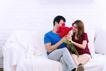 Love and valentine's day concept. Happy young couple holding beautiful bouquet red roses and heart together in living room. Cheerful smiling young women received bouquet of flowers from her boyfriend.