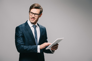 cheerful businessman in glasses using digital tablet isolated on grey