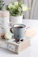 Cup of coffee with macarons, flowers, books and chocolate on the table
