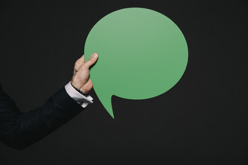 cropped view of man holding green speech bubble in hands isolated on black