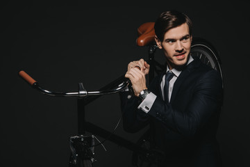 handsome businessman in suit holding bicycle in hands isolated on black