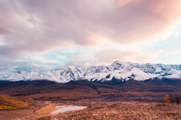 Pink and purple clouds over mountain range. Sunset or dawn in mountains in autumn. Hiking trip to valley of mountains.