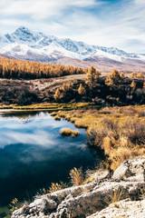 Fototapeta premium Reflection of mountains and clouds in clear surface of lake. Golden autumn in mountains.
