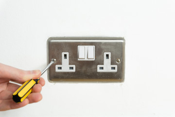 Screwdriver and Stainless steel UK plug socket on white wall