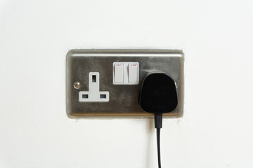 Stainless steel UK plug socket on white wall