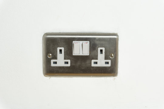 Stainless steel UK plug socket on white wall