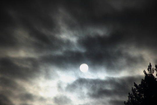 Dramatic white winter full moon behind the black clouds