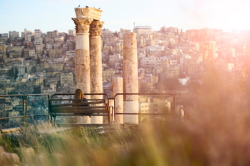 A girl is seated on a bench admiring the magnificent landscape from the Citadel of Amman in Jordan.