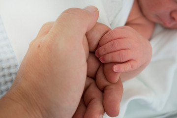 the newborn baby holds his dad's hand while he is asleep. A few hours after he was born.