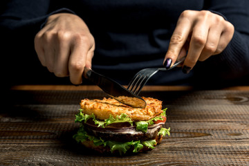 Healthy lifestyle, proper nutrition. Female hands cut a useful rice burger with vegetables, herbs and cutlet on a wooden board