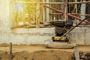 worker at sand ground compaction with vibration plate compactor machine. with a background is the structure of the construction of the building. with cement base and eucalyptus wood