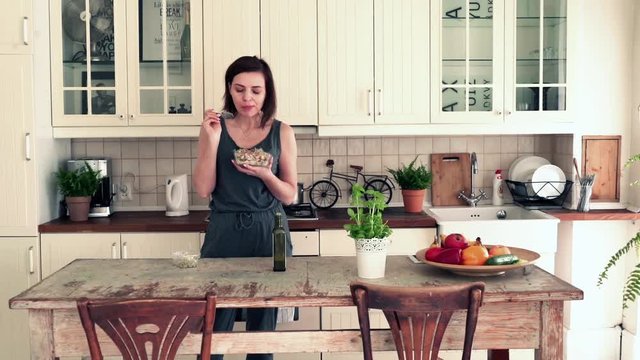 Young, beautiful woman trying delicious salad standing in the kitchen
