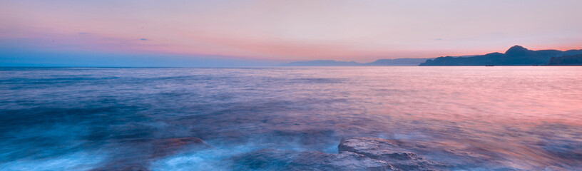 Fototapeta premium Beautiful mysterious marine landscape at sunset. Mountains, volcanic reef and ocean, panoramic banner.