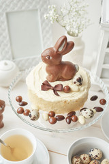 Rustic Easter Cake with Chocolate bunnies and Eggs. Easter greeting card background, closeup with copy space. Easter sweets for children. Chocolate bunny on decorated cake stand for Easter brunch.