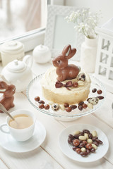 Obraz na płótnie Canvas Rustic Easter Cake with Chocolate bunnies and Eggs. Easter greeting card background, closeup with copy space. Easter sweets for children. Chocolate bunny on decorated cake stand for Easter brunch.