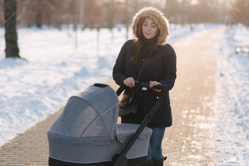 Mom walk with baby in pram. Winter park. Happy woman with her baby